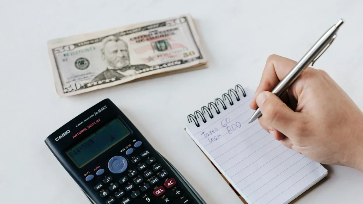 A person using a laptop and notebook to plan their weekly and monthly budget reset routine.